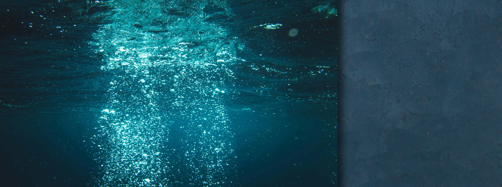 Unterwasseraufnahme, die Lichtstrahlen zeigt, die durch die Wasseroberfläche brechen und dabei leuchtende Blasen erzeugen.